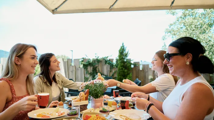 Gruppe von Frauen genießt Frühstück im Freien mit Gebäck, Käse und Kaffee